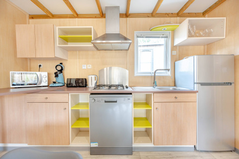 Cocina moderna con gabinetes de madera, lavavajillas, fregadero, nevera y electrodomésticos pequeños.