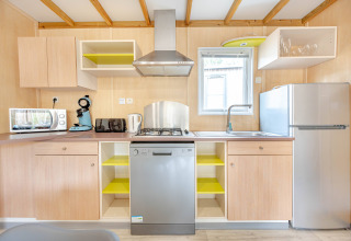 Cocina moderna con gabinetes de madera, lavavajillas, fregadero, nevera y electrodomésticos pequeños.