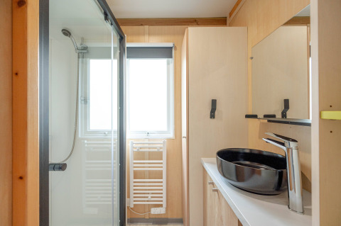 Baño moderno con ducha, lavabo negro y decoración de madera clara en Cottage Garden, Flower Camping Au Bois Des Biches, Francia.