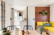 Intérieur de chalet lumineux et coloré avec canapé jaune, plantes et table à manger au Flower Camping Au Bois Des Biches.