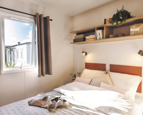 Lichte slaapkamer in Stacaravan Tribu bij Flower Camping Au Bois Des Biches in Frankrijk, met plank en raam.