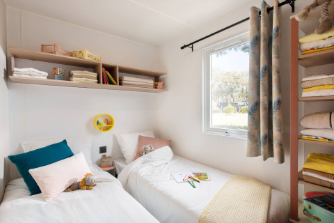 Lichte slaapkamer met twee bedden en planken in de Stacaravan Tribu op Flower Camping Au Bois Des Biches in Frankrijk.
