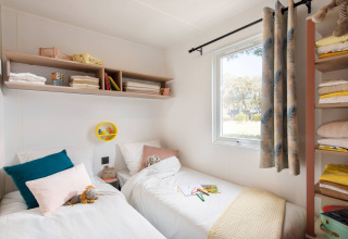 Lichte slaapkamer met twee bedden en planken in de Stacaravan Tribu op Flower Camping Au Bois Des Biches in Frankrijk.