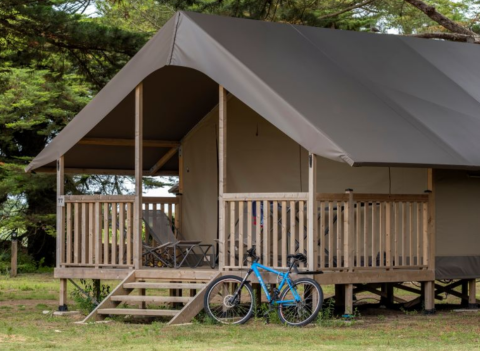 Safaritent met houten veranda, ligstoelen en blauwe fiets ervoor bij Flower Camping Monplaisir, Frankrijk.