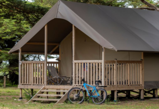 Safaritent met houten terras, ligstoelen en blauwe fiets ernaast op Flower Camping Monplaisir, Frankrijk.