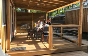 Familie sitzt auf der Holzterrasse eines Premium Mobilheims im Flower Camping La Canadienne in Frankreich.