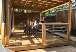 Familie sitzt auf der Holzterrasse eines Premium Mobilheims im Flower Camping La Canadienne in Frankreich.