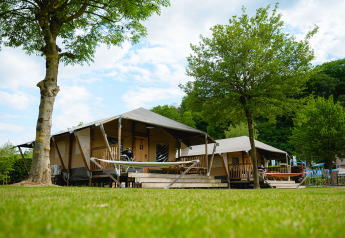 Tente safari Cottage avec terrasse et hamac sur un camping verdoyant entouré d’arbres et de verdure.