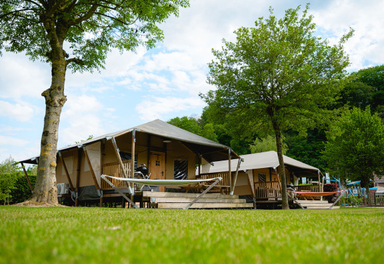 Tenda safari Cottage con veranda e amaca in un campeggio verde circondato da alberi e natura.