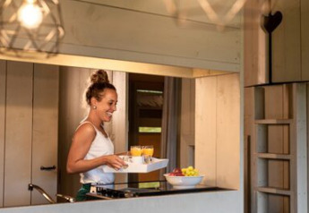 Une femme sert du jus et des fruits dans la cuisine de la tente Safari Cottage au camping 't Geuldal, Pays-Bas.