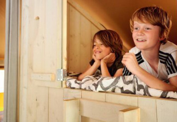 Two children relaxing inside a Safari tent Cottage at Campsite 't Geuldal in the Netherlands, smiling happily.