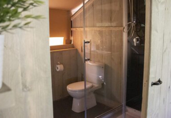Bagno con wc e doccia dietro una porta di vetro in una tenda safari al campeggio 't Geuldal.