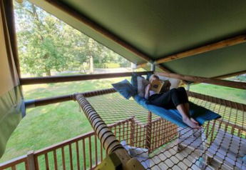 Person relaxing and reading on a hammock net inside a safari tent overlooking grassy fields in the Netherlands.