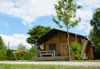 Tenda safari Nomad in campeggio, con terrazza in legno, panca, amaca e tanto verde sotto un cielo azzurro.