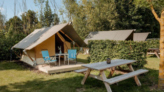 Safari Trekking Zelt auf einem Campingplatz mit Picknicktisch, Stühlen und viel Natur im Hintergrund.