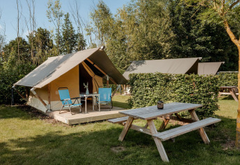 Safari Trekking Zelt auf einem Campingplatz mit Picknicktisch, Stühlen und viel Natur im Hintergrund.