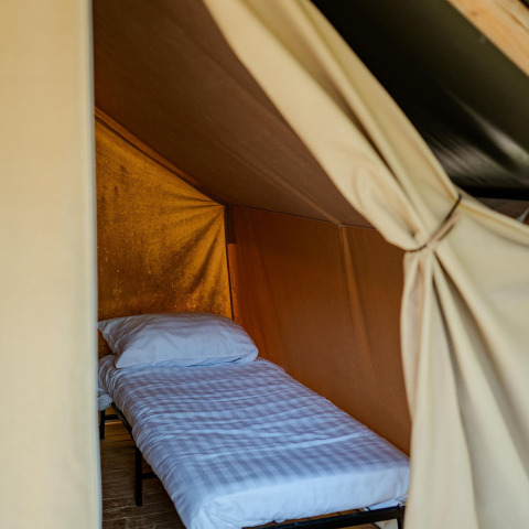 Binnenaanzicht van een eenpersoonsbed met wit beddengoed in een Safari Trekking tent op Camping 't Geuldal, Nederland.