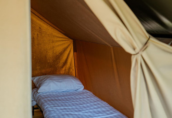 Interior view of a single bed with white bedding inside a Safari Trekking tent at Campsite 't Geuldal, Netherlands.