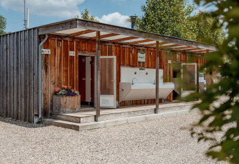 Outdoor sanitation building at Campsite 't Geuldal, Netherlands, with sinks, open doors, and wood walls.