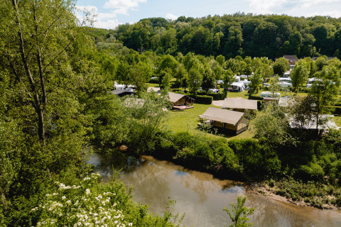 Vue sur des tentes safari près d'une rivière entourée d’arbres au camping 't Geuldal, Pays-Bas