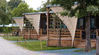 Foto di lodge accoglienti con verande in legno e vele ombreggianti, immersi in un ambiente verde e rilassante.