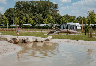 Een kind springt op stenen bij een vijver bij Limburg Lodge, Camping 't Geuldal, Nederland, met tenten op de achtergrond.