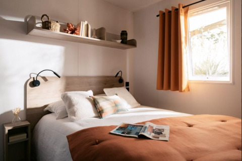 Gezellige slaapkamer in Limburg Lodge, Camping 't Geuldal, Nederland, met tweepersoonsbed en oranje gordijnen.