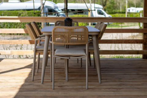 Buiteneethoek bij een lodge met houten terras, moderne tafel en stoelen, en campers op de achtergrond.