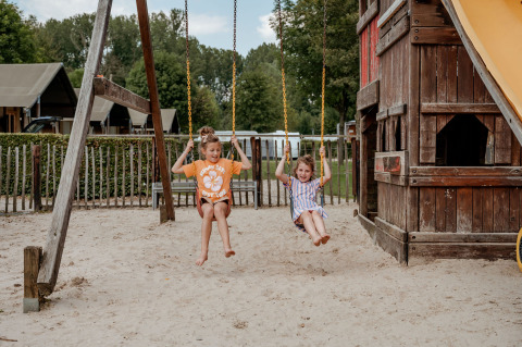 Twee kinderen schommelen op een speelplaats voor Limburg Lodge XL op Camping 't Geuldal in Nederland.