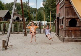 Twee kinderen schommelen op een speelplaats voor Limburg Lodge XL op Camping 't Geuldal in Nederland.