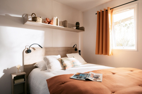 Lichte slaapkamer met tweepersoonsbed, oranje deken en zonlicht bij Limburg Lodge XL, camping 't Geuldal.
