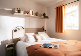 Lichte slaapkamer met tweepersoonsbed, oranje deken en zonlicht bij Limburg Lodge XL, camping 't Geuldal.