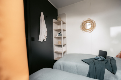 Kamer met twee bedden, grijze wand, plank, spiegel en badjas in Limburg Lodge XL, Camping 't Geuldal, Nederland.