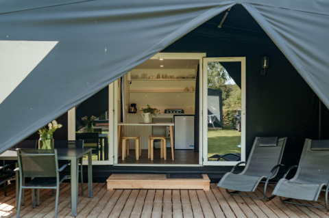 Ingang van de Coco Sweet safaritent met houten veranda, ligstoelen, eettafel en gezellige keuken binnen.
