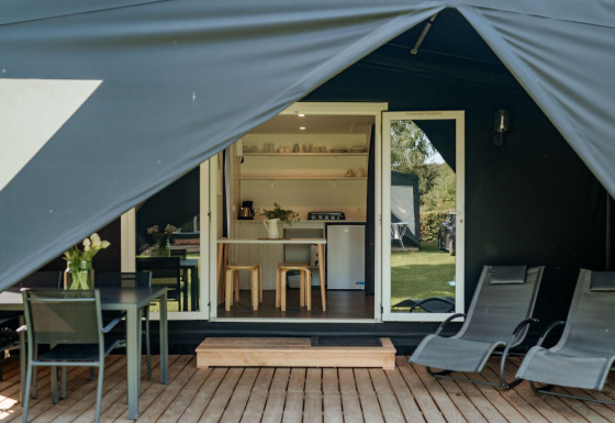 Ingang van de Coco Sweet safaritent met houten veranda, ligstoelen, eettafel en gezellige keuken binnen.