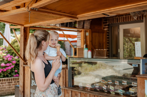 Een moeder en kind genieten van een ijsje bij een houten kiosk bij de Coco Sweet safari tent op Camping 't Geuldal.