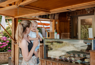 Een moeder en kind genieten van een ijsje bij een houten kiosk bij de Coco Sweet safari tent op Camping 't Geuldal.