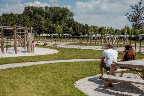 Ouders kijken naar hun kind bij de speeltuin van de Coco Sweet safaritent op Camping 't Geuldal, Nederland.
