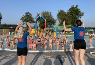 Niños juegan y participan en actividades en una piscina guiados por dos instructoras en un glamping.