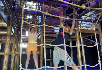 Deux enfants jouent sur une structure d’escalade intérieure pendant leur séjour en hébergement glamping.