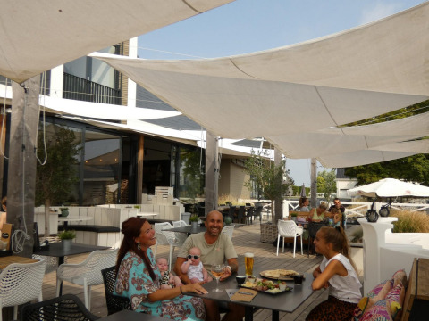 Gezin geniet van een maaltijd onder schaduwzeilen op het terras bij een glampingverblijf, ontspannen sfeer.