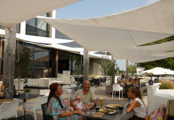 Gezin geniet van een maaltijd onder schaduwzeilen op het terras bij een glampingverblijf, ontspannen sfeer.