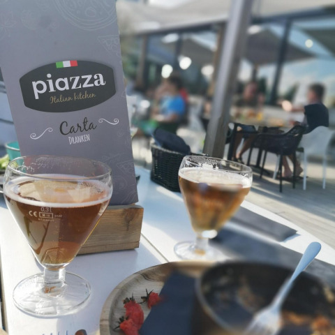 Foto op terras van glamping met menukaart van Piazza Italian Kitchen, drankjes en eten op tafel.