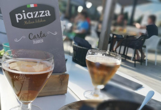 Foto op terras van glamping met menukaart van Piazza Italian Kitchen, drankjes en eten op tafel.