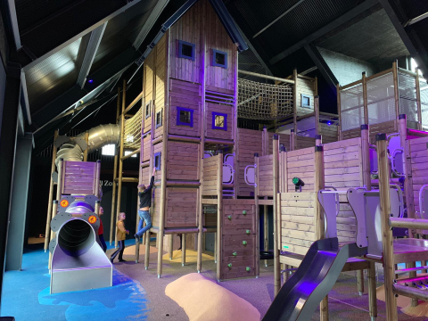 Binnen speeltuin met houten constructies en spelende kinderen bij een glampingverblijf.