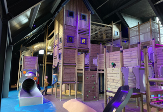 Binnen speeltuin met houten constructies en spelende kinderen bij een glampingverblijf.