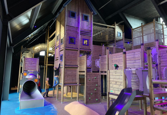 Binnen speeltuin met houten constructies en spelende kinderen bij een glampingverblijf.