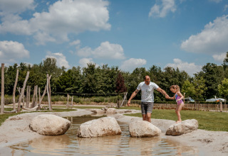 Man en meisje balanceren op stenen in een beekje op Camping 't Geuldal in Limburg, Nederland.