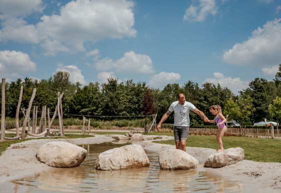Man and girl balance on rocks in a stream at Campsite 't Geuldal holiday park in Limburg, Netherlands.