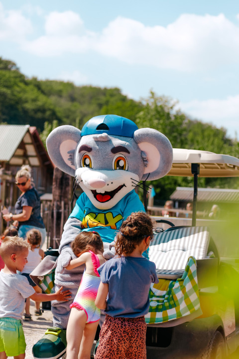 Children hugging a mouse mascot at Campsite 't Geuldal holiday park in Limburg, Netherlands, on a sunny day.
